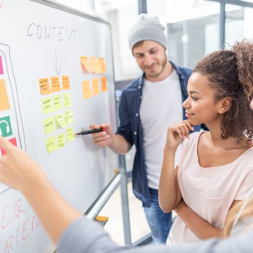 Male and female employee using a whiteboard and post-it notes to plan content.